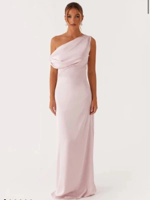 Ljusrosa långklänning oneshoulder - Elegant ljusrosa långklänning med oneshoulder-design och draperad överdel. Klänningen har en smickrande, figurnära passform och är tillverkad i ett mjukt, glansigt material som ger en lyxig känsla. Perfekt för speciella tillfällen.