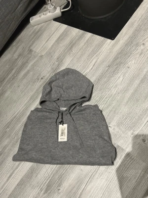 Grå hoodie från RYVLS - Storlek 158-164 Snygg grå hoodie från RYVLS med klassisk huva och dragsko. Tillverkad i mjukt material som känns skönt mot huden. Perfekt för en chill och avslappnad stil. Enkel design utan tryck eller mönster, passar till det mesta.