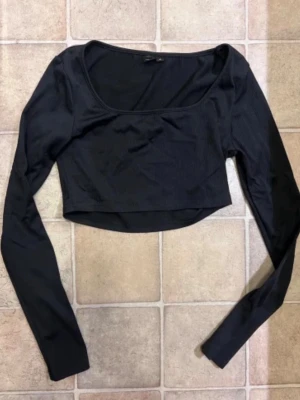Svart croppad långärmad topp - En svart, croppad topp med lång ärm och rundad urringning. Toppen har en slim passform och är tillverkad i ett stretchigt material som sitter snyggt på kroppen. Perfekt att styla med höga jeans eller kjol.
