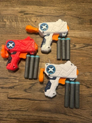 Nerf gun två vita och en röd  - Säljer tre leksakspistoler i plast, två vita och en röd. Alla har orange avtryckare och medföljer totalt nio skumpilar med blå toppar. Perfekt för roliga dueller med vänner.