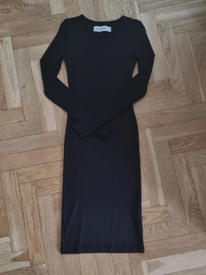 Svart ribbad klänning från Ivyrevel - Snygg svart ribbad klänning från Ivyrevel i modellen Aliana. Klänningen har en kroppsnära passform och är tillverkad i ett stretchigt material med elastan. Perfekt för dig som gillar stilrena och enkla plagg med en modern touch.