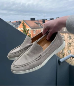 Charles tyrhwhitt loafers - Snygga loafers i beige mocka med klassisk design och vit gummisula. Skorna har en stilren och enkel look med diskreta sömmar och låg profil. Perfekta för dig som gillar en clean och avslappnad stil.