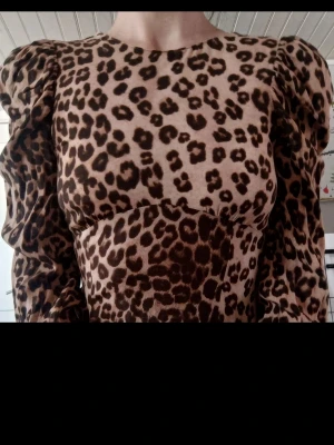 Leopardmönstrad långklänning med puffärm - Snygg medel långklänning med leopardmönster och markerade puffärmar. Klänningen har rund halsringning och är figurnära upptill med lång ärm. Perfekt för dig som vill sticka ut med ett djurmönstrat plagg.