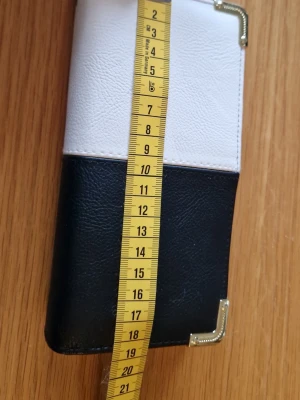 Svartvit plånbok med metallhörn - Snygg plånbok i svart och vitt konstläder med rektangulär form och dekorativa metallhörn. Plånboken är cirka 17 cm lång och 9 cm bred, perfekt för kort och sedlar. Stilren design som passar till många olika looks.