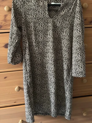 Leopardmönstrad klänning från Amisu - Cool leopardmönstrad klänning från Amisu med trekvartsärm och rak passform. Klänningen har v-ringning och är i mjukt, stretchigt material som känns skönt mot huden. Perfekt för dig som vill sticka ut med ett djurmönster!