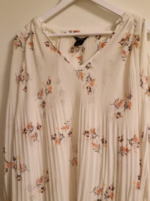 Vit blommig långärmad blus Lindex - Superfin vit blus från Lindex med blommigt mönster i orange och lila toner. BLUSEN har v-ringning, långa ärmar med resår vid ärmslut och är gjord i ett lätt, plisserat material som ger ett luftigt intryck. Perfekt för vår och sommar!