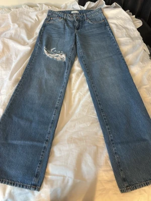 Blåa wide leg jeans med slitning - Säljer ett par blåa wide leg jeans med en snygg slitning på ena låret. Jeansen har klassisk femficksdesign och raka, vida ben. Aldrig använda💛