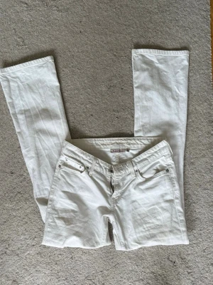 Vita bootcut jeans - Snygga vita jeans från Levi’s med bootcut och lågmidjad passform . Dom är använda en del gånger och har några defekter, därav priset. På baksidan av benen är det små stänk fläckar som jag inte lyckats få bort i tvätten, det syns på den sista bilden! De syns knappt. Skriv för fler bilder eller mått.