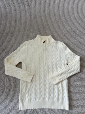 Vit stickad tröja med halv dragkedja - Stickad vit tröja med hög krage och halv dragkedja framtill. Långa ärmar och ribbade muddar vid ärmslut och nederkant. Perfekt för lager-på-lager och en clean look. Den passar för storlek L