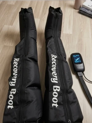 Recovery Boot kompressionsstövlar - Svarta kompressionsstövlar från Recovery Boot med tillhörande digital kontrollenhet. Perfekta för återhämtning efter träning, med dragkedjor längs hela benen och tydlig vit text. Tillverkade i slitstarkt syntetmaterial.