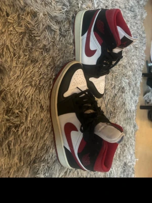 Air Jordan 1 Retro High OG röd/vit/svart - Säljer ett par Air Jordan 1 Retro High OG med klassisk färgkombination i rött, vitt och svart. Skorna har högt skaft, svart Swoosh och röda detaljer. Ovandelen är i läder och textil, med ikonisk Jumpman-logga på plösen. Perfekta för dig som gillar streetwear och sneakerskultur.