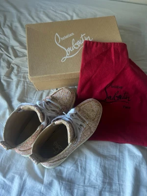 Glittriga Christian Louboutin sneakers - Säljer ett par glittriga sneakers från Christian Louboutin med vit sula och klassisk röd undersida. Skorna har färgglatt glitter över hela ovandelen, vita skosnören och en rund logotyp på sidan. Kommer med originalkartong och dustbag. De har använts men mycket sällan. 