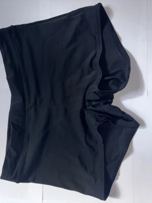 Svarta träningsshorts från Lindex - Säljer ett par svarta träningsshorts från Lindex. De är av mjukt och stretchigt material som sitter skönt mot kroppen. Perfekta att ha under en kort kjol eller klännings.