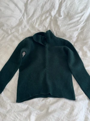 Mörkgrön stickad tröja Massimo Dutti - Mysig mörkgrön stickad tröja från Massimo Dutti med hög krage och långa ärmar. Tröjan är tillverkad i mjukt material och har en enkel, stilren design som passar perfekt till höst och vinter.