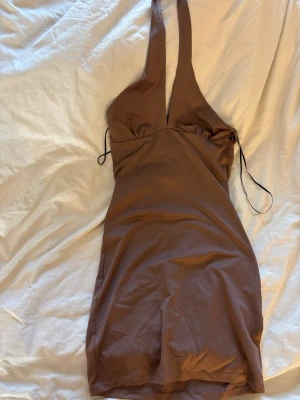 Brun halterneck klänning hm - Snygg brun kort klänning från HM med halterneck och djup v-ringning. Klänningen har smala knytband i ryggen och är figurnära i modellen. Perfekt för dig som vill ha en trendig och stilren look.