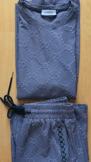 Grått set GG-mönster - Säljer ett grått set från Gucci med tydligt GG-mönster i tyget. Setet består av en T-shirt och matchande shorts med resår i midjan och svarta snören. Perfekt för dig som gillar exklusiv och bekväm stil. Aldrig använt. 