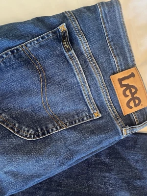 Blå bootcut jeans från Lee - Snygga blå bootcut jeans från Lee med klassisk femficksdesign och bruna kontrastsömmar. Jeansen har en normal midja och är tillverkade i slitstark denim. Perfekta för dig som gillar tidlösa bootcut jeans!