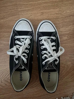 Svarta Converse All Star låga sneakers - Klassiska svarta Converse All Star sneakers med vit tå och vita snören. Skorna har vit sula med svart rand och tydlig logga bak. Tillverkade i canvas med gummisula. Perfekta för en avslappnad och cool stil.