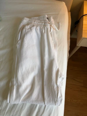 Vita linnebyxor från lager 157 - Säljer ett par vita linnebyxor från lager 157 med resår i midjan och dragsko. Byxorna har sidofickor och är gjorda i ett mjukt och bekvämt material, perfekta för chill dagar. Enkel och clean design som passar till det mesta.