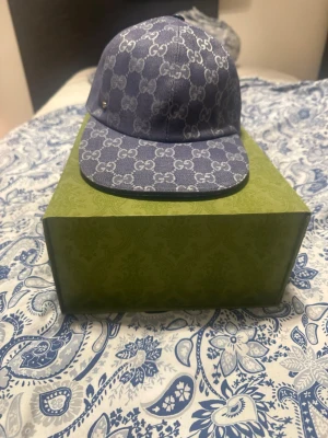 Blå GG-monogram keps från Gucci - Snygg blå keps från Gucci med klassiskt GG-monogram över hela kepsen. Kepsen har böjd skärm och är tillverkad i canvasmaterial med ljus insida. Perfekt accessoar för att lyfta din streetwear-look. Kan mötas upp i Göteborg eller frakta