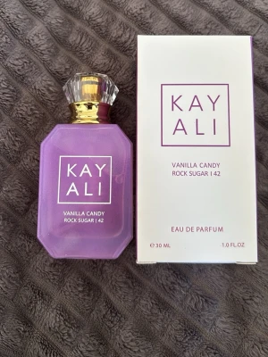 Kayali Vanilla Candy Rock Sugar 42 EdP - Kayali Vanilla Candy Rock Sugar 42 Eau de Parfum i en lila, multifacetterad glasflaska med gulddetaljer och kristalliknande kork. Doften kommer i en matchande vit och lila kartong. Flaskan rymmer 30 ml och har en modern, lyxig design.Engast 1 gång spreyad på handen för lukta.Priset går diskutera 