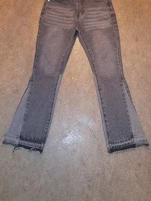 Gallery dept byxor gråa  - Säljer ett par gråa jeans från Wrangler med rak passform och hög midja. Jeansen har råa, fransiga benslut och klassiska fem fickor. Materialet är denim i bomull och färgen är tvättad grå med slitningar för en cool vintagekänsla.