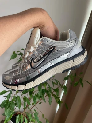 Nike P6000 - Ny pris : 2879 kr                                                      Mitt pris 1249                                                        Snygga sneakers från Nike i silver med svart swoosh och detaljer i mesh och syntet. Skorna har en chunky beige och svart sula med tydligt mönster för bra grepp. Perfekt för dig som gillar en futuristisk och sportig look.