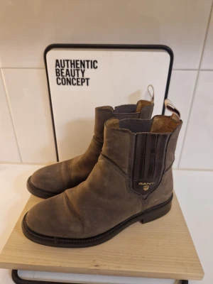 Bruna Chelsea boots från Gant - Säljer ett par snygga Chelsea boots från Gant i brunt läder. Klassisk modell med elastiska paneler på sidorna och dragflikar bak. Robust sula och stilren design som passar till många outfits. Perfekta för dig som gillar tidlös och avslappnad stil.