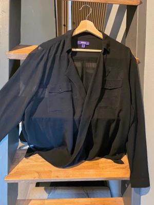 Svart transparent blus från Mexx - Snygg svart transparent blus från Mexx med lång ärm och två bröstfickor. Blusen har en avslappnad passform och djup v-ringning framtill. Perfekt att styla lager på lager eller med ett linne under. Tunn och luftig i materialet. Strl 44, passar 40 och 42
