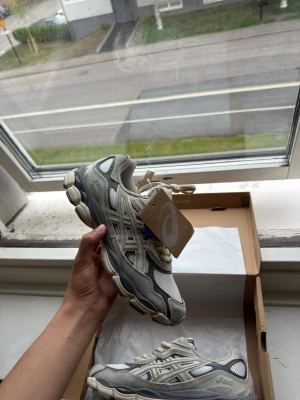 Asics gel nyc cream oyster grey 42 storlek - Snygga Asics sneakers i grått och vitt med chunky sula och meshdetaljer. Skorna har klassisk Asics-logga på sidan och coola retrovibbar. Perfekta för dig som gillar streetwear och sportig stil.