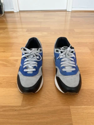 Nike Air Max 1 Essential – Storlek 41 - Säljer ett par Nike Air Max 1 Essential i snygg blå/grå/svart färgkombination i storlek 41. Skorna är i bra använt skick och har fortfarande mycket kvar att ge. Väldigt bekväma sneakers som passar perfekt både till vardags och streetwear. Normal användning och mindre slitage finns, men överlag är de välhållna. Air Max-sulan ger bra komfort och modellen är en tidlös klassiker från Nike.