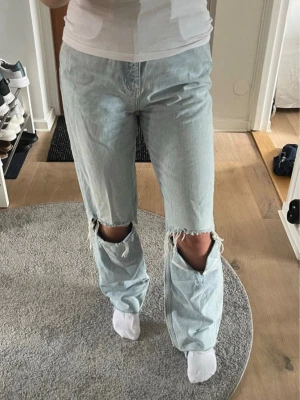Jeans med slitningar  - Ljusblå jeans med slitningar vid knäna från Gina Tricot. Rak/vid passform med oversized känsla och längre ben. Snygg tvätt i blekt denim och väldigt trendiga. Använda få gånger och i fint skick.   Är uppsydda vid anklarna för att passa mig som är 155cm, men går enkelt att sprätta upp lm man vill ha jeansen längre (för dig som är runt 160/165cm). Dessa är i storlek L men skulle säga att dom sitter mer som än M!🤍