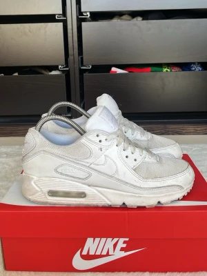 Nike Air Max 90 vita sneakers - Säljer ett par klassiska Nike Air Max 90 sneakers i helvitt. Skorna har mesh och läderdetaljer, ikonisk Air Max-sula och snygga paneler. Perfekt för dig som gillar stilrena och sportiga sneakers med retrovibe.