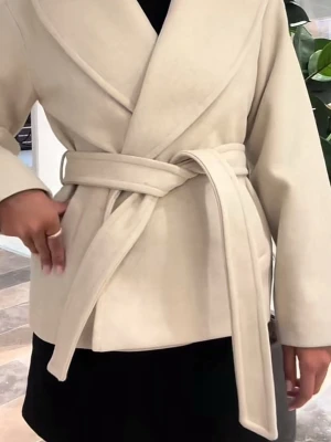 Beige kappa med knytskärp - Stilren beige kappa med bred krage och knytskärp i midjan. Kappan har en rak passform och är tillverkad i ett mjukt material som ger en lyxig känsla. Perfekt för dig som vill ha en enkel men trendig look.