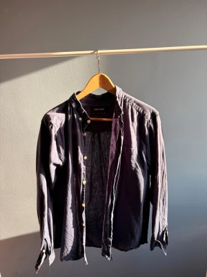 Mörkblå skjorta från Lyle & Scott - Stilren mörkblå skjorta från Lyle & Scott med klassisk krage och knappar framtill. Skjortan har lång ärm och är tillverkad i mjuk bomull, perfekt för en avslappnad men snygg look. Perfekt nu till sommaren!🙌🏼