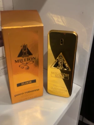 Paco Rabanne Million Elixir parfym - Exklusiv parfym från Paco Rabanne, Million Elixir. Flaskan är guldglänsande med en rektangulär form och har en elegant svart och guld logotyp på framsidan. Förpackningen är också guld med matchande design. Perfekt för dig som vill sticka ut med en lyxig doft.