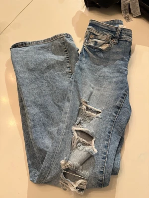 Ljusblå ripped jeans från Aeropostale - Säljer ett par ljusblå jeans från Aeropostale med slitningar och hål på benen. Jeansen har klassisk femficksdesign, knapp och dragkedja samt raka ben. Perfekt för dig som gillar en avslappnad och trendig look.