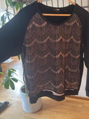 Svart spetsmönstrad hoodie Maison Scotch - Snygg svart hoodie från Maison Scotch med unik spetsmönstrad framsida i vågigt mönster. Tröjan har rund halsringning och långa ärmar i slätt material. Perfekt för dig som vill ha en hoodie med lite extra detaljer och stil.