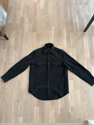 Svart overshirt från A Day's March - Stilren svart overshirt från A Day's March i storlek medium. Sjukt passande till sena sommarkvällar, inga defekter eller liknande. Nypris~1600. Hör av dig vid frågor🙃 Med vänlig hälsning, Avenue 