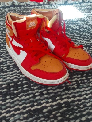 Nike Air Jordan zoom High röd/orange - Säljer ett par Nike Air Jordan 1 High sneakers i rött, orange och vitt. Skorna har klassisk hög siluett, röda snören och detaljer, vit sula och ikoniska Swoosh-loggan på sidan. Tillverkade i läder med Zoom Air-märke på plösen och Jordan Wings-logga på ankeln.