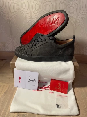 Christian Louboutin svarta spikes sneakers - Säljer ett par svarta sneakers från Christian Louboutin med klassiska röda sulor och coola spikes på tån. Skorna är i mocka och har svarta skosnören. Perfekta för dig som vill sticka ut med en edgy och lyxig stil.
