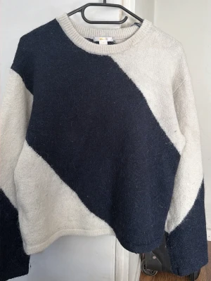 Stickad tröja från Gina Tricot - Säljer en stickad tröja från Gina Tricot med breda diagonala blockmönster i mörkblått och ljusgrått. Tröjan har rund halsringning och långa ärmar. Materialet är mjukt och fluffigt, perfekt för kalla dagar.
