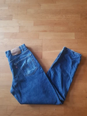 Levi's 550  - Säljer ett par klassiska blå Levi's 550 blåa jeans med hög midja och raka ben. Jeansen har en vintage look med slitningar på bakfickan och rå kant vid benslutet. Tillverkade i kraftig denim med den ikoniska röda Levi's-lappen på fickan.