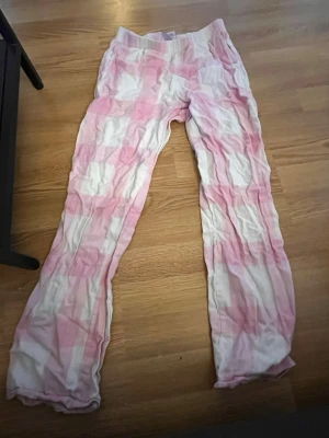 Rosa och vita rutiga pyjamasbyxor - Mysiga pyjamasbyxor i ett mjukt material med rosa och vita rutor. Byxorna har resår i midjan och raka ben, perfekta för chillkvällar hemma. Passar dig som gillar en avslappnad och bekväm stil.