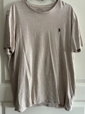 Beige t-shirt från Polo Ralph Lauren - Säljer en stilren beige t-shirt från Polo Ralph Lauren med klassisk rund halsringning och diskret logga broderad på bröstet. T-shirten är kortärmad och gjord i mjuk bomull för en skön känsla. Perfekt till jeans eller shorts! 