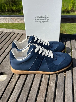 Blå Maison Margiela gats - Maison Margiela sneakers i blått med vita detaljer och klassiska gum-yttersulor. Skorna har en låg profil, vita snören och kombinerar mocka och läder för en stilren look. Perfekta för dig som vill ha något exklusivt och trendigt. 0bs; lnte 0rglnal, men mycket bra kvalitet 😊
