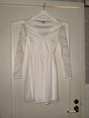 Vit spetsklänning från Bubbleroom xxs  - Supersöt vit klänning från Bubbleroom med långärmade spetsärmar och v-ringning. Överdelen har ett vackert spetsmönster medan kjolen är slät och faller fint. Perfekt för student eller firande.