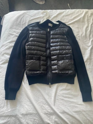 Svart dunjacka från Moncler - Svart Moncler cardigan jacka med DIST-certifierat dun. Jackan är glansig och har QR kod som går till moncler hemsidan. Jackan är i storlek 4, hade sagt att det är en M men passar även mig som har S. Köpt på plick för 2500 i höstas men kommer inte till användning längre. 