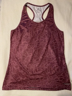 Vinrött träningslinne från North Bend - Snyggt vinrött träningslinne från North Bend med geometriskt mönster. Linnet har brottarrygg och är gjort i ett snabbtorkande, stretchigt material som passar perfekt till gymmet eller löprundan.