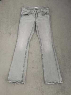 Grå bootcut jeans från Gina Tricot - Säljer ett par grå bootcut jeans från Gina. Jeansen har en ljusgrå tvätt. Lite slitna i benkanten med inget stort.